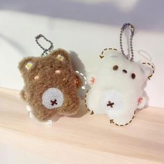 two stuffed animals are hanging from key chains on a shelf together, one is brown and the other is white