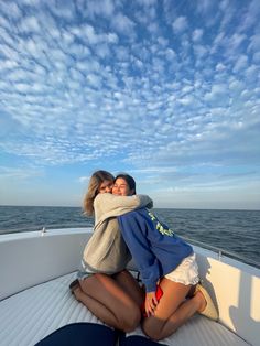 two women are sitting on the back of a boat in the ocean hugging each other