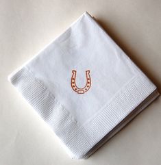 a white napkin with an orange horseshoe embroidered on the front and bottom, sitting on a table