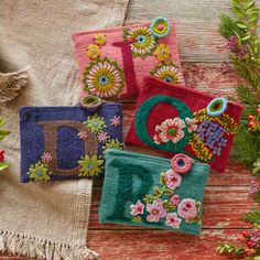 four embroidered purses sitting on top of a wooden table next to flowers and greenery