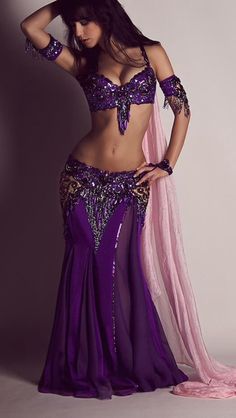 a woman in a purple belly dance outfit posing with her hands on her hips and wearing a pink veil