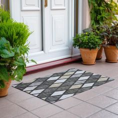 two potted plants are sitting on the front porch next to a white door with a black and gray checkered rug