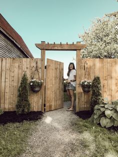 a woman standing at the entrance to a wooden gate with potted plants on either side