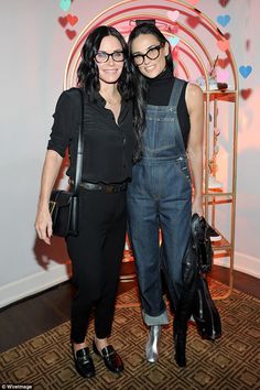 two women standing next to each other in overalls