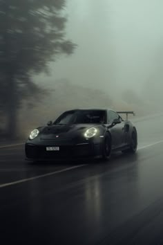 a black sports car driving on a wet road in the rain with fog behind it