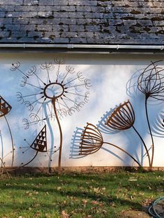 a large metal wall with dandelions painted on it's side in front of a house