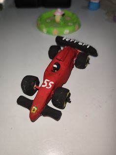 a red toy race car sitting on top of a white table next to a green object