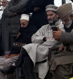 two men sitting next to each other while looking at a cell phone in front of them