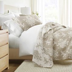 a bed with white and beige comforters in a bedroom next to a window on a rug