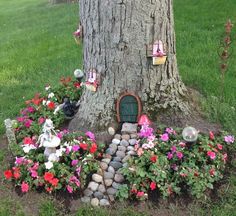 there is a tree with flowers around it and a gnome's house in the middle