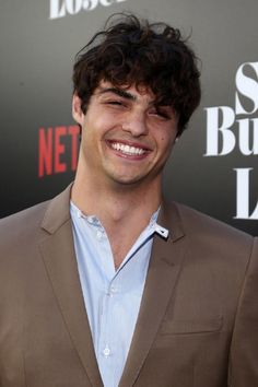 a smiling young man in a brown suit and blue shirt