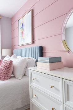 a bedroom with pink walls, white furniture and a mirror on the wall above it