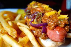 a hot dog on a bun with chili and cheese next to french fries