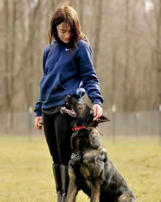 a woman standing next to a dog on top of a grass covered field