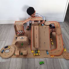 a young boy playing with a cardboard race track set on the floor in front of a white wall