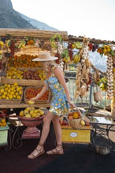 a woman in a dress and straw hat standing next to a fruit stand