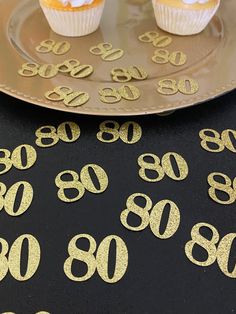 some cupcakes are sitting on a plate with gold numbers and confetti