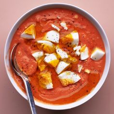 a white bowl filled with soup topped with boiled eggs and cheese on top of a pink surface