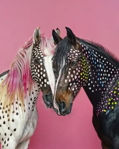 two horses standing next to each other in front of a pink wall with polka dots