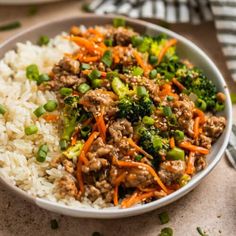 a bowl filled with rice, meat and veggies next to a fork on a table