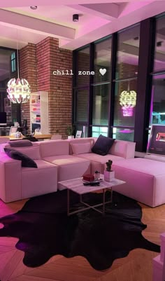 a living room filled with lots of furniture next to large windows and pink lighting on the ceiling