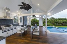 an outdoor kitchen and dining area next to a swimming pool with a fan on the ceiling