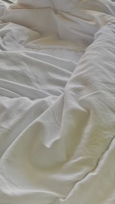 an unmade bed with white sheets and pillows