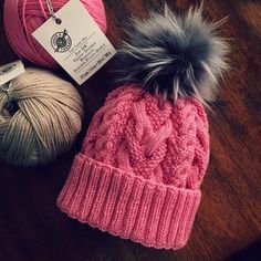 two balls of yarn and a knitted hat on a wooden table next to each other