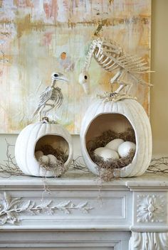 two white pumpkins sitting on top of a mantel covered in fake birds and skeletons