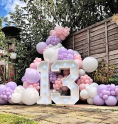 the number thirteen is surrounded by balloons and streamers in front of a wooden fence