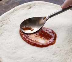 a person spooning ketchup onto a pizza dough