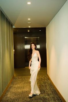 a woman in a white dress is walking down the hallway