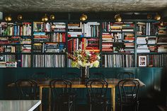 a dining room table with chairs and bookshelves in front of it on the wall