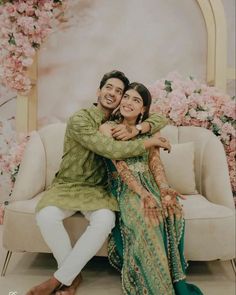 a man and woman sitting next to each other on a couch in front of flowers