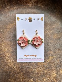 a pair of earrings with pink flowers on them sitting on top of a piece of wood