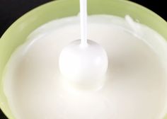 a green bowl filled with milk and a white spoon sticking out of the liquid in it