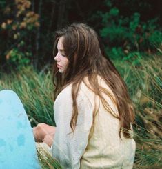 a woman sitting in the grass with a blue surfboard