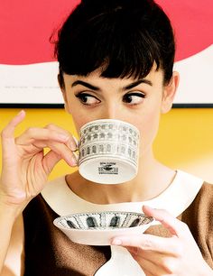 a woman drinking from a coffee cup with money in front of her face and holding a plate