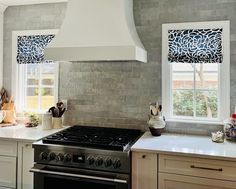 a stove top oven sitting inside of a kitchen next to a window with roman shades