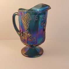 a blue glass pitcher sitting on top of a metal stand next to a white wall