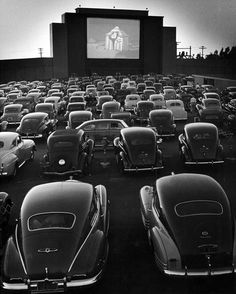 an outdoor movie theater with rows of cars parked in front of it and people watching