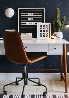 a white desk topped with a computer monitor next to a lamp and potted plant