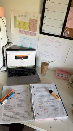 a laptop computer sitting on top of a desk next to an open book and coffee cup