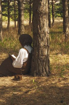 a person sitting under a tree in the woods with a book on it's lap