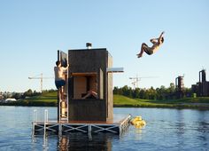 two people are jumping into the water from a floating house that is on stilts