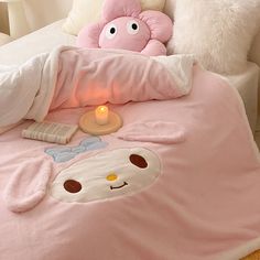 a bed with a pink comforter and pillows on top of it next to a lit candle