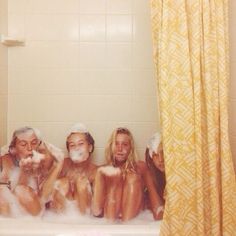 four women sitting in a bathtub with soap on their faces