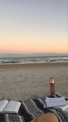 an open book is sitting on top of a blanket at the beach while someone reads