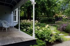 a white chair sitting on top of a wooden porch next to a lush green garden