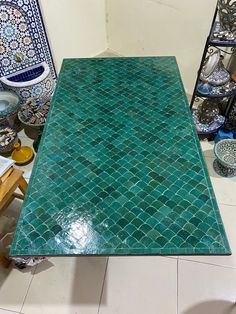 a table that is covered in green tile and surrounded by vases on the floor